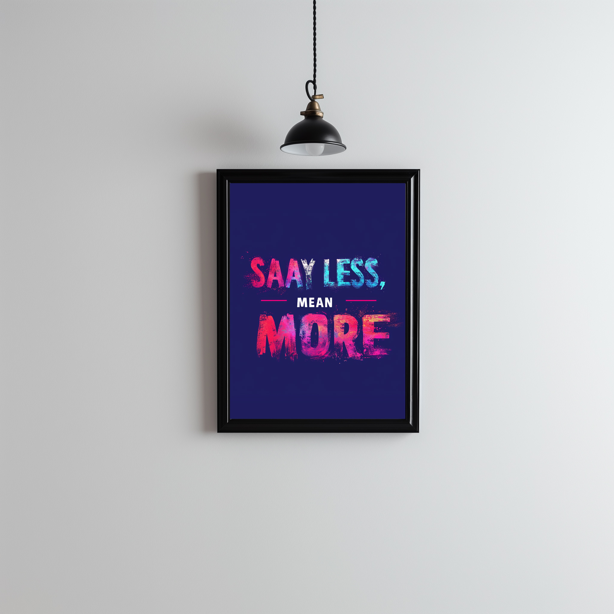 framed print with a bold quote that says 'Say Less, Mean More' in colorful letters on a dark background. It’s hanging on a plain wall with a light above it.